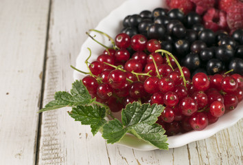Fresh berries (raspberry, red currant, black currant) in glass bowl on wooden table