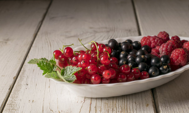 Fresh berries (raspberry, red currant, black currant) in glass bowl on wooden table