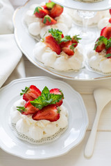 Homemade small strawberry pavlova meringue cakes with mascarpone cream and fresh mint leaves on white plate