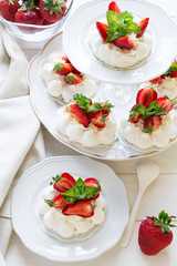 Homemade small strawberry pavlova meringue cakes with mascarpone cream and fresh mint leaves on white plate