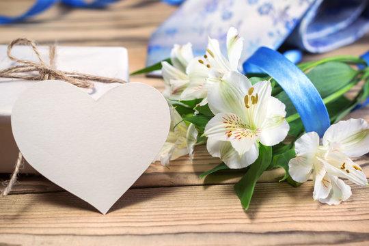 Gift box, flowers, card, ribbon and tie on wooden table