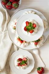 Homemade small strawberry pavlova meringue cakes with mascarpone cream and fresh mint leaves on white plate