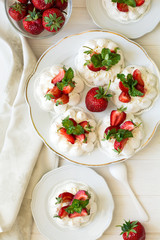 Homemade small strawberry pavlova meringue cakes with mascarpone cream and fresh mint leaves on white plate