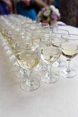 Rows of champagne glasses on table with beautiful bouquet on colorful tablecloth and rustic wooden wall at background. Wedding ceremony