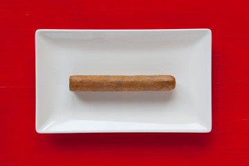 White ceramic dish with luxury Cuban cigar on over red backgroun