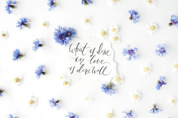 inspirational quote "what is done in love is done well" written in calligraphy style on paper with cornflowers and chamomiles isolated on white background. Flat lay, top view