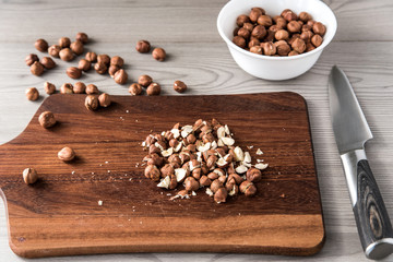 Cut hazelnuts on a wooden board with a knife, ingredients for cooking, wood background, top view