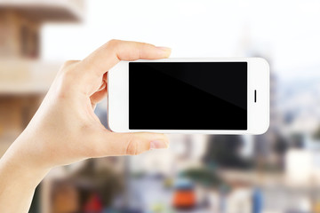 Hand shows mobile smart phone, urban city blurred background