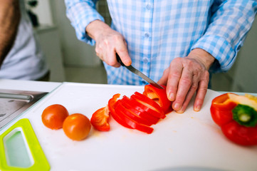 Hands of unrecognizable senior woman cutting red pepper.