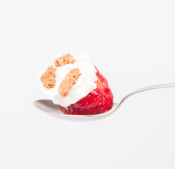 Strawberry with whipped cream and granola on a spoon on a white background
