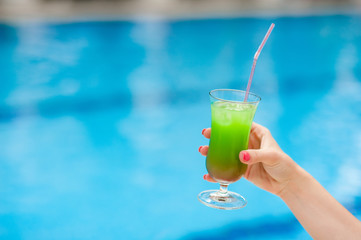 Bright cocktail in a female hand near the pool