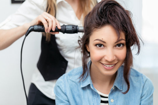 Professional hairdresser doing hairstyle to young woman 