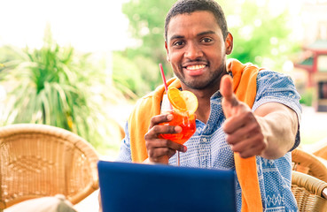 Cheerful afro american man thumb up sitting at restaurant - Black guy holding cocktail glass showing okay hand sign in beach bar cafe - Concept of relaxing travel holiday and successful lifestyle
