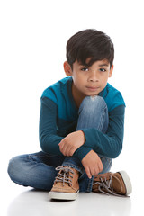 Full length portrait of a young mixed race boy sitting on the floor. Isolated on white.