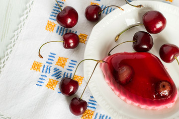 Naklejka na ściany i meble Fruity a jelly. Fruity a jelly on a plate and fresh sweet cherries on a napkin on a light wooden background.