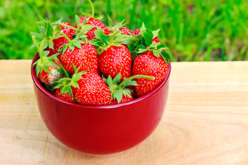 Fresh, organic strawberry in bowl, on wooden table, outdoors.