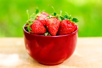 Fresh, organic strawberry in bowl, on wooden table, outdoors