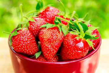 Fresh, organic strawberry in bowl, on wooden table, outdoors