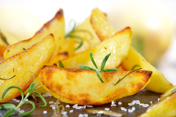 Knuspige Kartoffelspalten mit Rosmarin auf einem alten Schneidebrett aus Holz  serviert - Crispy potato wedges with rosemary served on an old wooden cutting board