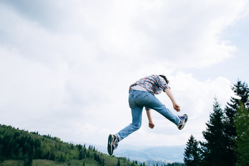 Young man Jumping Outdoors on rock in mountains sky