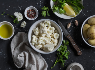 Raw ingredients - cauliflower, potatoes, olive oil and spices on a dark stone background