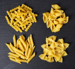 Various types of pasta on black background, from above