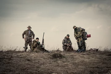 Crédence de cuisine en verre imprimé Chasser Hunters standing together against sunset sky in rural field during hunting season