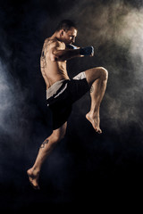 Muscular kickbox or muay thai fighter punching in jump. Smoke.