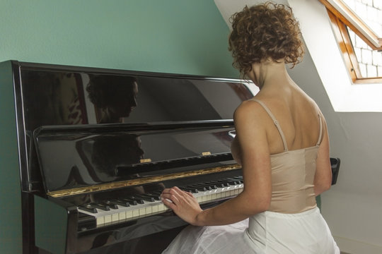 Rear view ballerina performing and playing the piano in a house