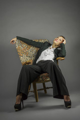 Fototapeta premium Young sensual woman in men's black suit sit in an armchair