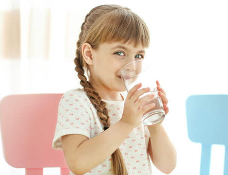 Cute little girl drinking water on light background