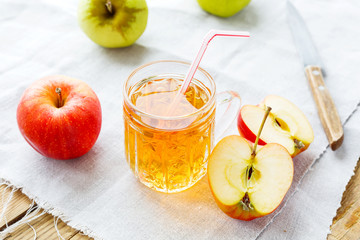 Rustic background with apples and apple juice in glass on homespun napkin.