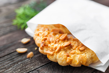 Tasty tart with peanuts in white paper bag. Rustic wooden background with sweet dessert.