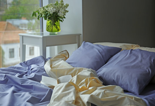 Unmade bed with crumpled blue bed linens and book