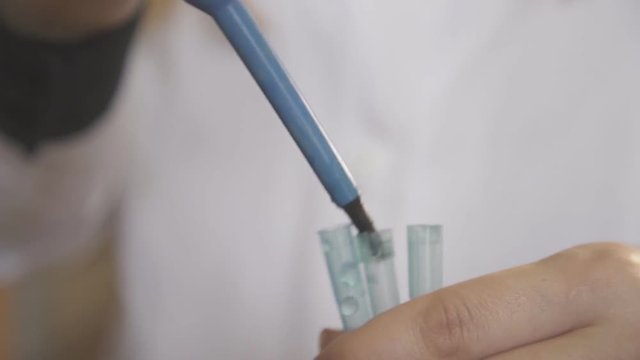 Woman chemist using a pipette pours liquid into test tubes.