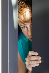 Serious teen peeking from between door and wall