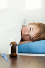 Obraz na płótnie Canvas Sick boy laying under thick blanket on bed
