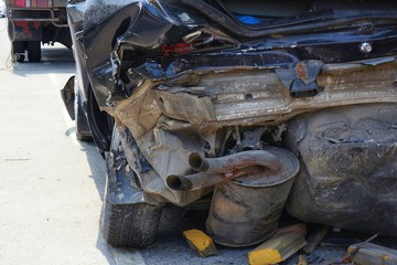 Fototapeta premium Demolished Rear Part of Dark Car after Accident. Destroyed Body, damaged tires, exhausting pipe, luggage space, bumper.