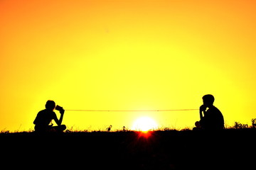 Silhouette children playing string phone at sky sunset