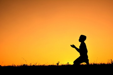 silhouette of a boy who praying over at sunset