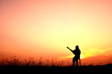 Naklejka na ściany i meble Silhouette women playing guitar in the sunset