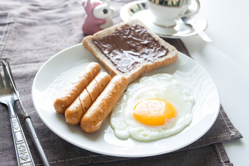 Plate of breakfast with egg, sausages, bread and chocolate cream