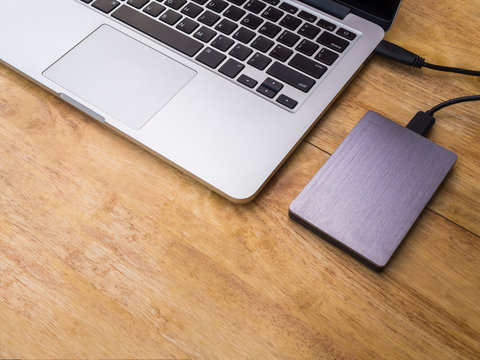 External or portable hard drive (HDD) connected to laptop computer for transfer or backup data on wooden texture office desktop with copy space
