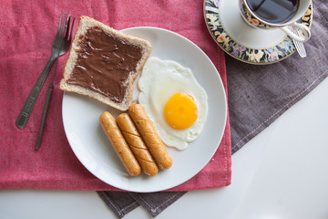 Plate of breakfast with egg, sausages, bread and chocolate cream