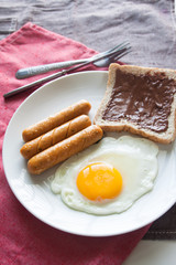 Plate of breakfast with egg, sausages, bread and chocolate cream