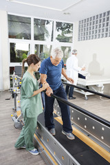 Physiotherapist Standing By Patient Walking Between Parallel Bar