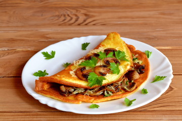 Ruddy scrambled eggs with cheese, fried mushrooms and parsley. Omelet with filling on a plate on wooden background. Fried mushrooms are laid out on an omelet. Leaves of parsley laid on a plate.