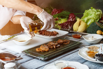 Hand holding bottle with liquid. Liquid dripping on cooked meat. Olive oil for veal medallions. Delicious meat cooked at restaurant.
