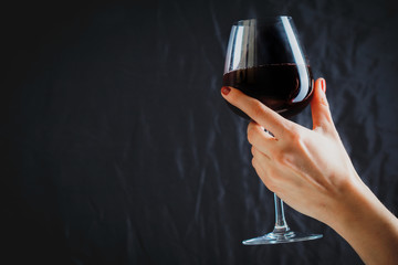 Hand holding glass of red wine on dark grey background