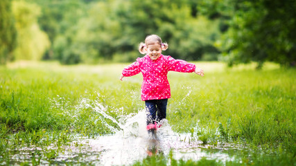 happy child girl running and jumping in puddles after rain